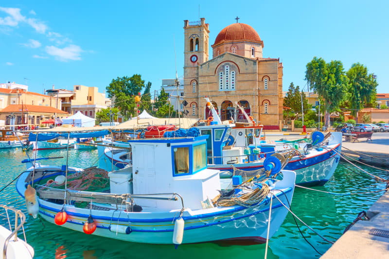 Athens base in Greece with a boat on the water and architectural building in the background.