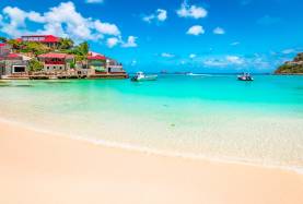 St Martin base showing azure blue waters on a beach with a bright blue sky with a couple boats on the water